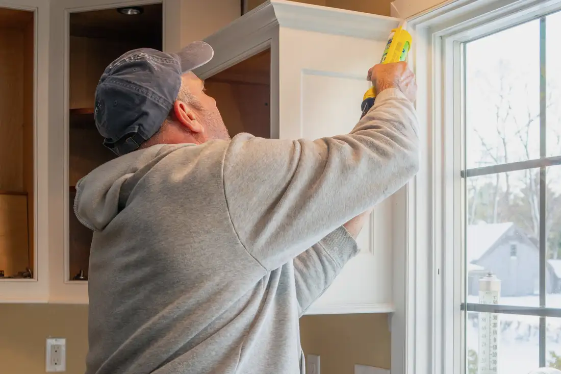 Carpenter caulking a kitchen cabinet