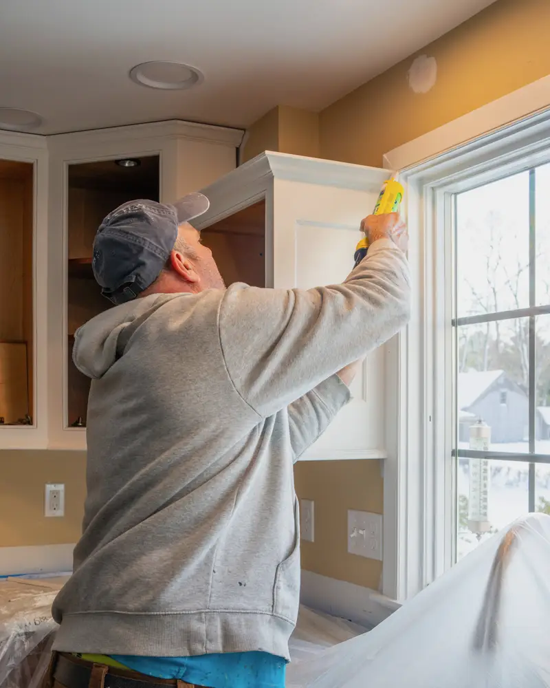 Carpenter caulking a newly installed kitchen cabinet