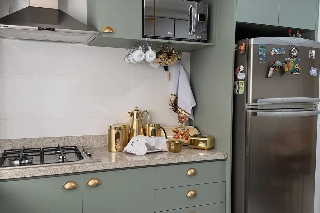 Sage green kitchen with white counters and brass hardware